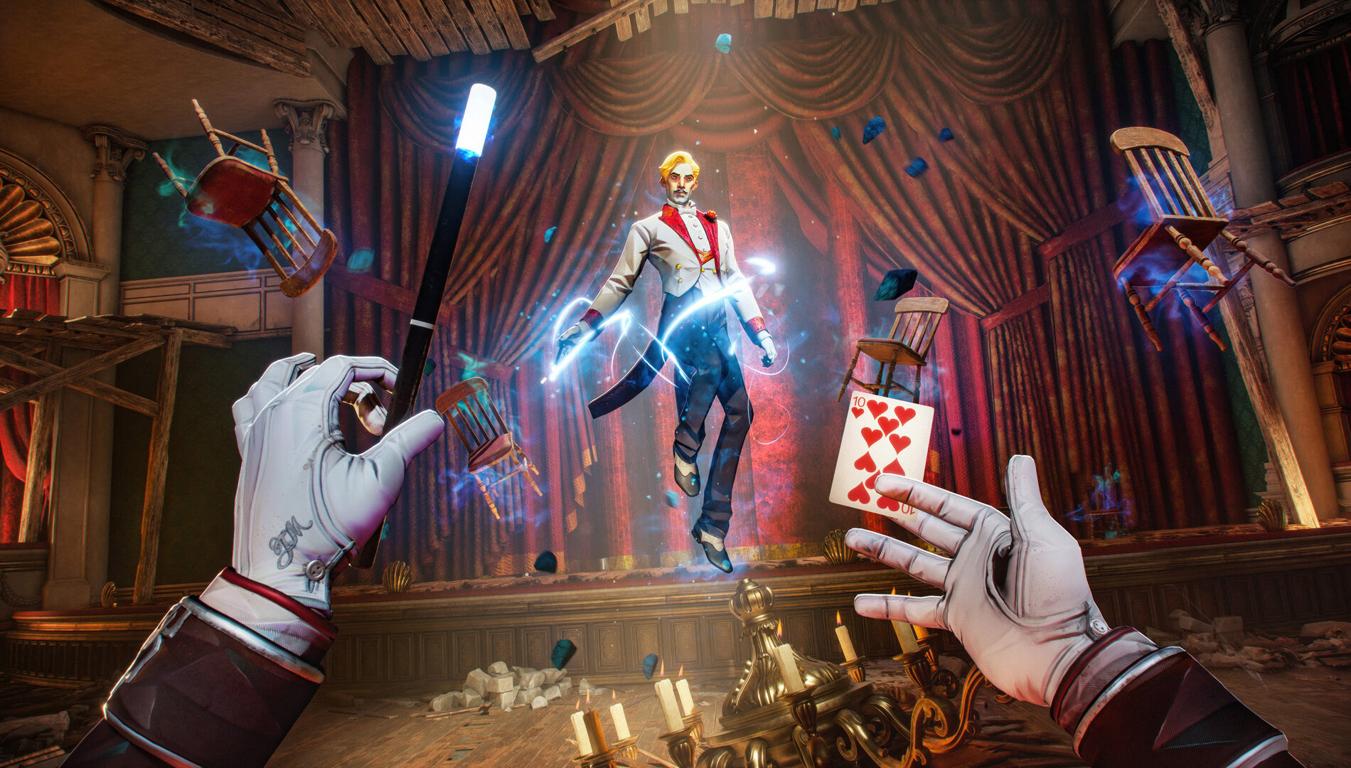 Captura de tela em perspectiva de primeira pessoa de um jogo de ação e mágica. A visão do jogador mostra duas mãos vestindo luvas brancas formais e elegantes; a mão esquerda segura uma varinha mágica preta com a ponta iluminada por uma luz azul brilhante, enquanto a mão direita está aberta, com uma carta de baralho (dez de copas) flutuando logo acima dos dedos. No centro do cenário, um mágico inimigo de cabelos loiros, usando um terno de gala branco e vermelho (fraque), flutua no ar envolto em uma aura de energia mágica azul e faíscas. O combate acontece no palco de um teatro antigo e decadente, com grandes cortinas vermelhas ao fundo. Cadeiras de madeira e pedaços de entulho flutuam no ar ao redor devido ao efeito de levitação, e um lustre dourado quebrado com velas repousa no chão de madeira em primeiro plano.