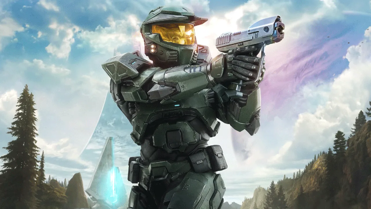 Imagem promocional do personagem Master Chief, do jogo de ficção científica Halo. Em plano médio, o supersoldado usa sua icônica armadura MJOLNIR verde-oliva com detalhes em preto e um capacete com visor dourado reflexivo e brilhante. Ele está de perfil para a direita, empunhando uma pistola Magnum prateada com as duas mãos em posição de mira. O cenário de fundo apresenta uma paisagem alienígena com montanhas cobertas por florestas de pinheiros, sob um céu azul claro com nuvens brancas e um brilho solar difuso. À esquerda, ergue-se uma estrutura futurista pontiaguda com luzes azuis e, cruzando o céu ao fundo, destaca-se a imensa curvatura anelar característica de um planeta-anel (Halo Array).